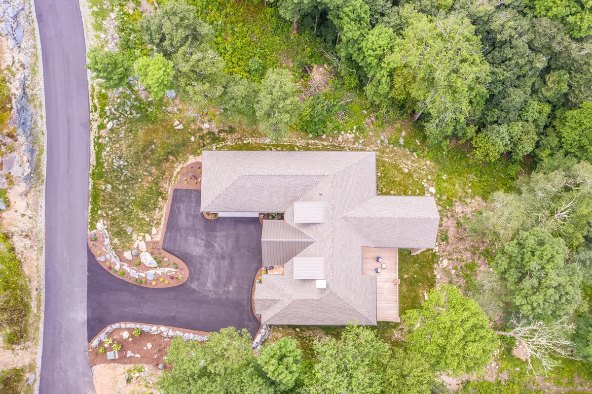 The image displays the home’s exterior, driveway, and the enveloping trees, with the deck visible as a social hub. The setting captures the sense of peace and seclusion, while also indicating space for outdoor gatherings or easy access to hiking trails.