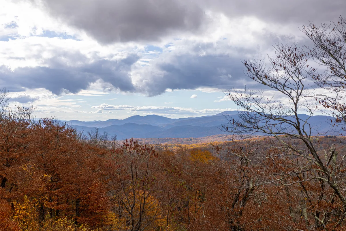 A sweeping view of the mountain range with lush foliage under a cloudy sky, capturing the breathtaking natural scenery that defines Sugar Mountain during the summer. It evokes the spirit of exploration, adventure, and seasonal beauty.