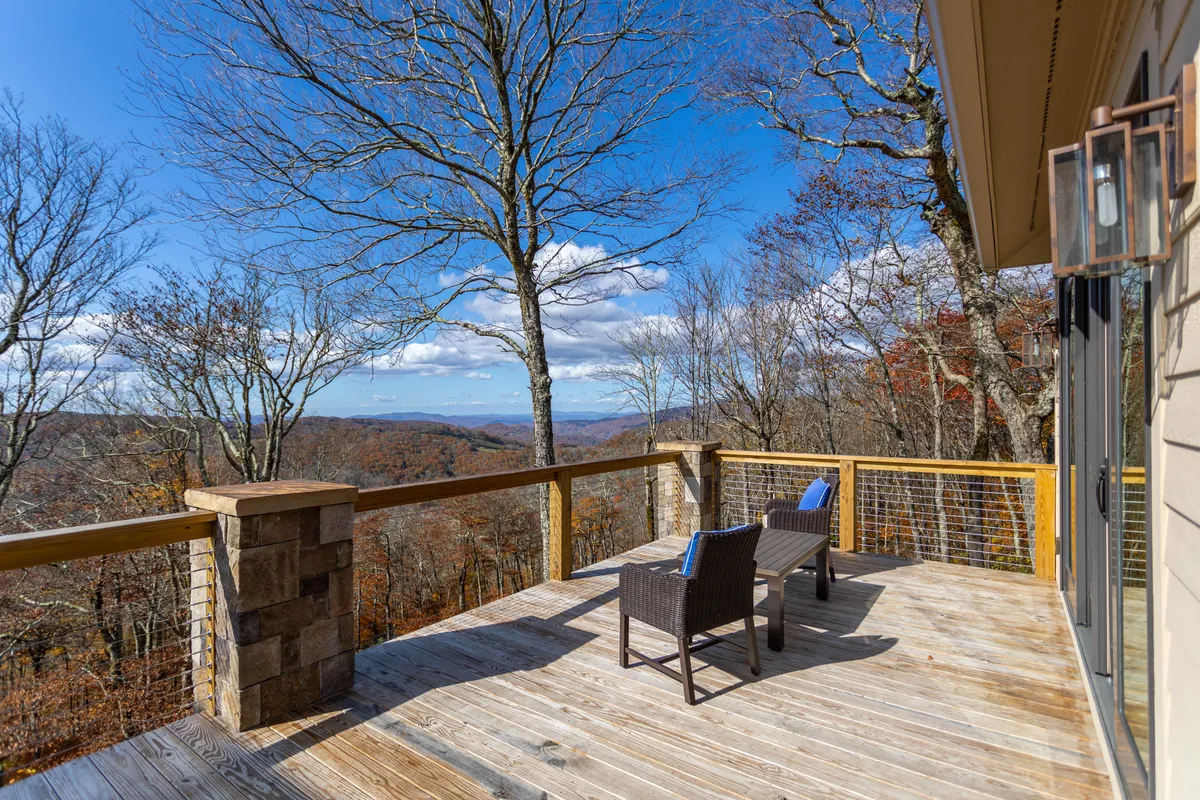 An inviting wooden deck features two comfortable chairs overlooking a sweeping mountain landscape. The outdoor setting is serene and surrounded by trees, creating the perfect backdrop for al fresco dining, morning coffee, or evening relaxation. The deck’s orientation emphasizes the direct connection between home and the natural beauty of Banner Elk.