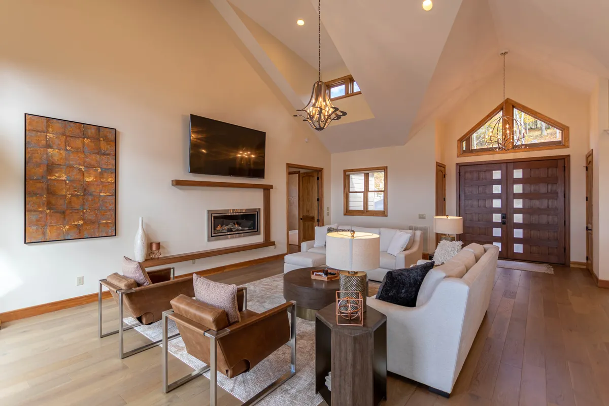 An inviting seating area with a beautiful fireplace, cozy chairs, and expansive windows letting in natural light. An art piece and warm decor create a space ideal for intimate gatherings and relaxation by the fire.