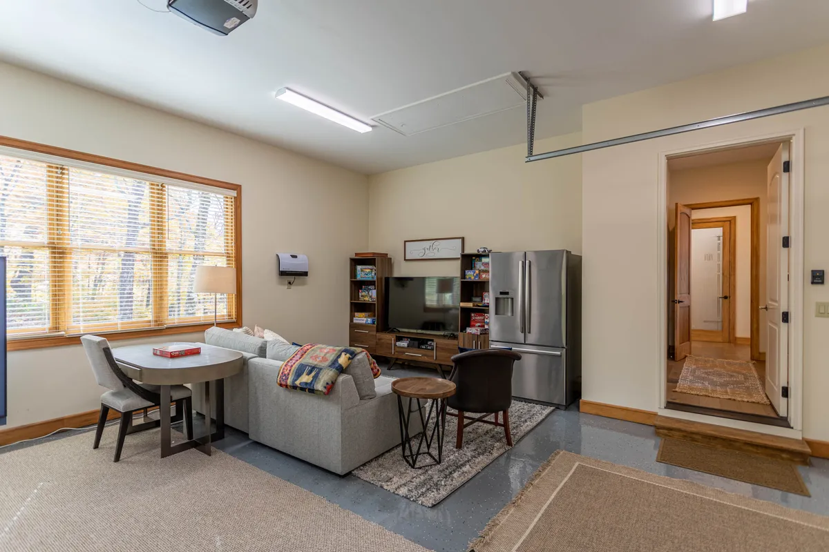 A cozy living area featuring a sofa, television, dining table, and windows that allow natural light into the room. The setup invites relaxation, movie watching, and group social activities, which complements the idea of a home entertainment hub.