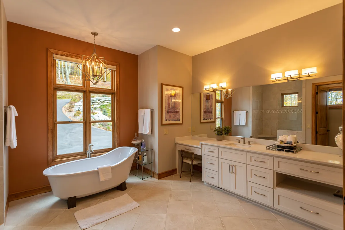 A spa-inspired bathroom with a freestanding bathtub under a sparkling chandelier, double vanity, and large window flooding the space with natural light. The design merges modern luxury with a sense of calm, perfect for relaxation and self-care.