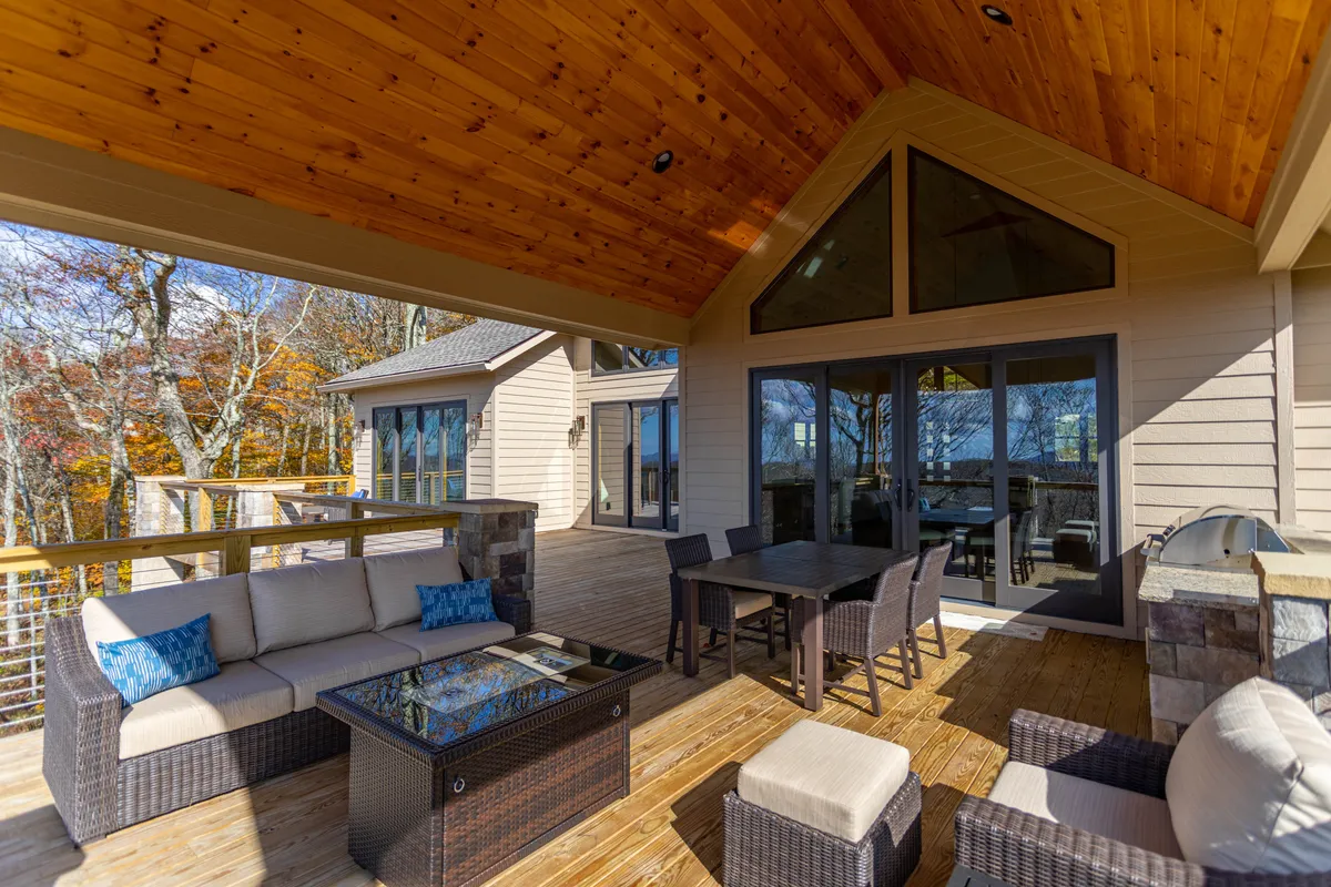 This image features a welcoming outdoor seating area and dining table set against the backdrop of the home's large windows. Surrounded by trees, the area invites guests to enjoy fresh air, connect with nature, and easily flow between indoor and outdoor entertainment zones.