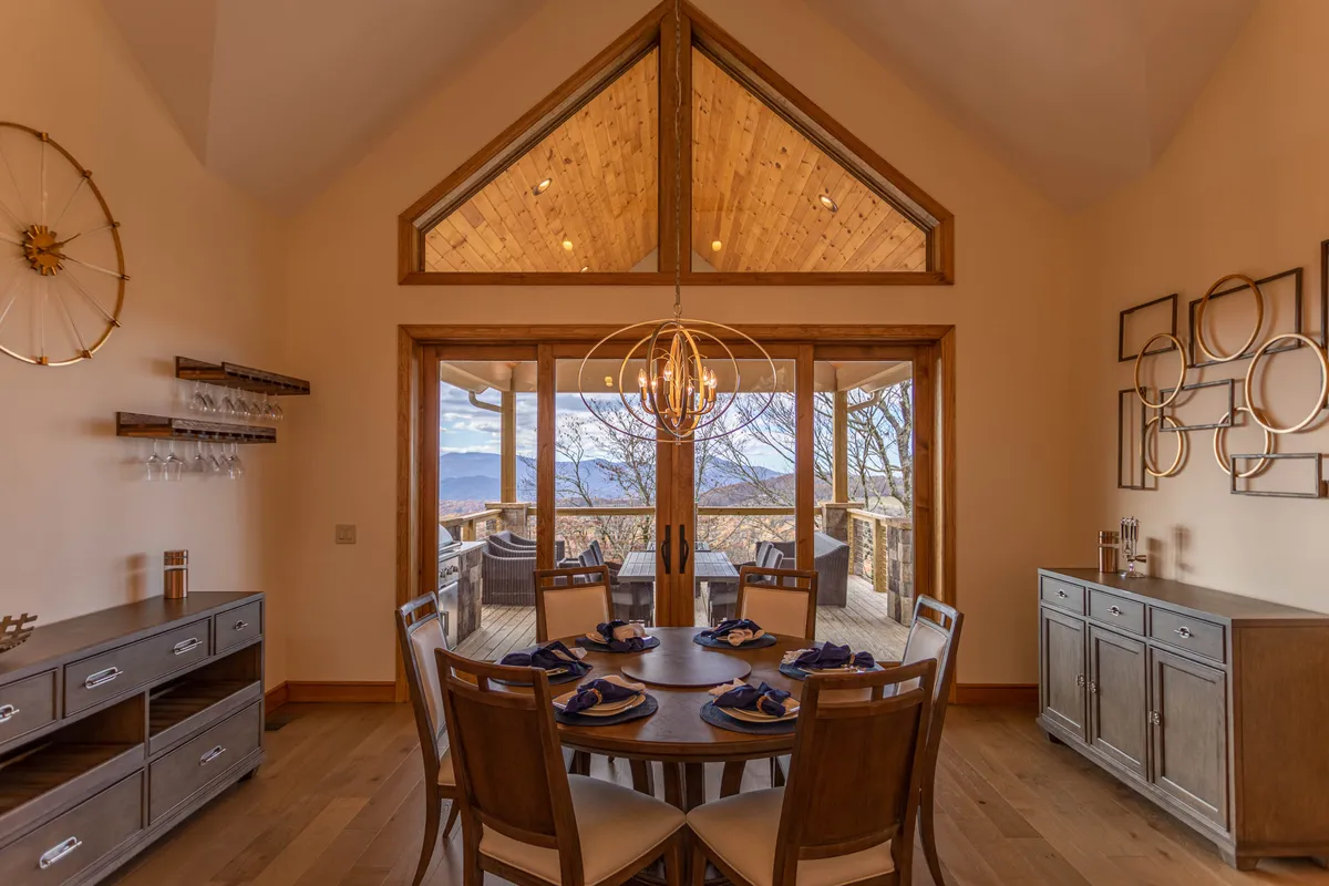 This image captures a dining table perfectly positioned in front of expansive windows with breathtaking mountain views. The elegant chandelier and tasteful wall art create an upscale yet welcoming atmosphere, while the table is set for a meal, inviting gatherings and celebrations. The visual connection between indoor dining and the surrounding landscape underscores the allure of dining with a view.